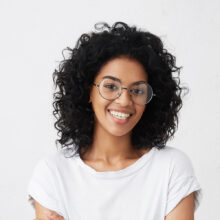 Indoor shot of beautiful happy African American student girl standing isolated in white studio smiling cheerfully, keeping her arms folded, relaxing indoors after morning lectures at university